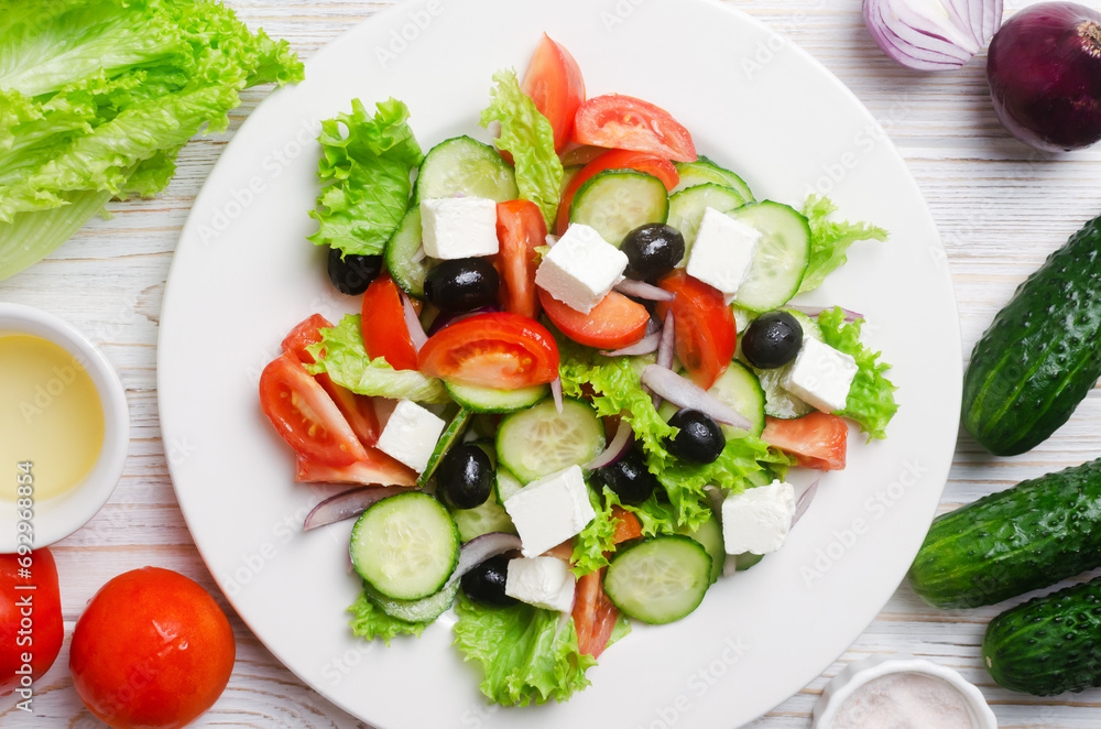 Classic Greek salad with cucumbers, tomatoes, red onion, feta cheese, lettuce and black olives on a white wooden table. The concept of traditional dishes. Simple ingredients. Top view.
