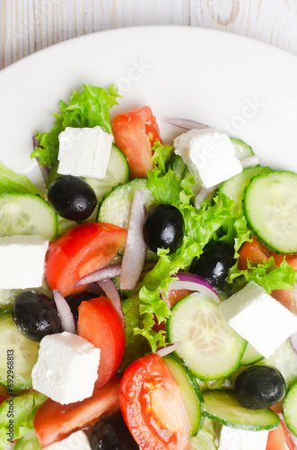 Classic Greek salad with cucumbers, tomatoes, red onion, feta cheese, lettuce and black olives on a white wooden table. The concept of traditional dishes. Simple ingredients. Top view.