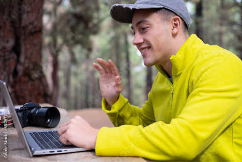 Young beautiful boy freelancer using video conference while working on laptop computer from remote. Hipster traveler working distantly while enjoying nature mountain landscape during vacations © luciano