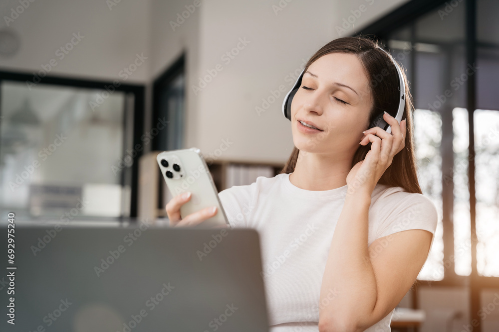 Smiling girl relaxing at home, she is playing music using smartphone tablet, laptop, and wearing white headphones. Smiling girl relaxing at home, she is playing music using smartphone tablet, laptop, and wearing white headphones.