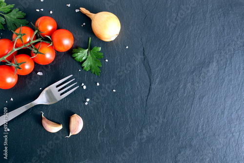 A fork with fresh vegetables and a place for text lie on a black stone board.