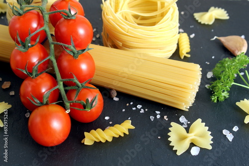Several pieces of round pasta with red tomatoes lie on a black background.