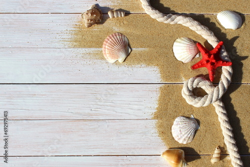 On a wooden white table lies sea sand and various shells with a rope.