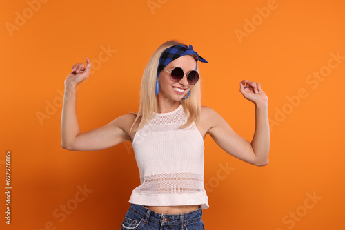Portrait of smiling hippie woman in sunglasses on orange background