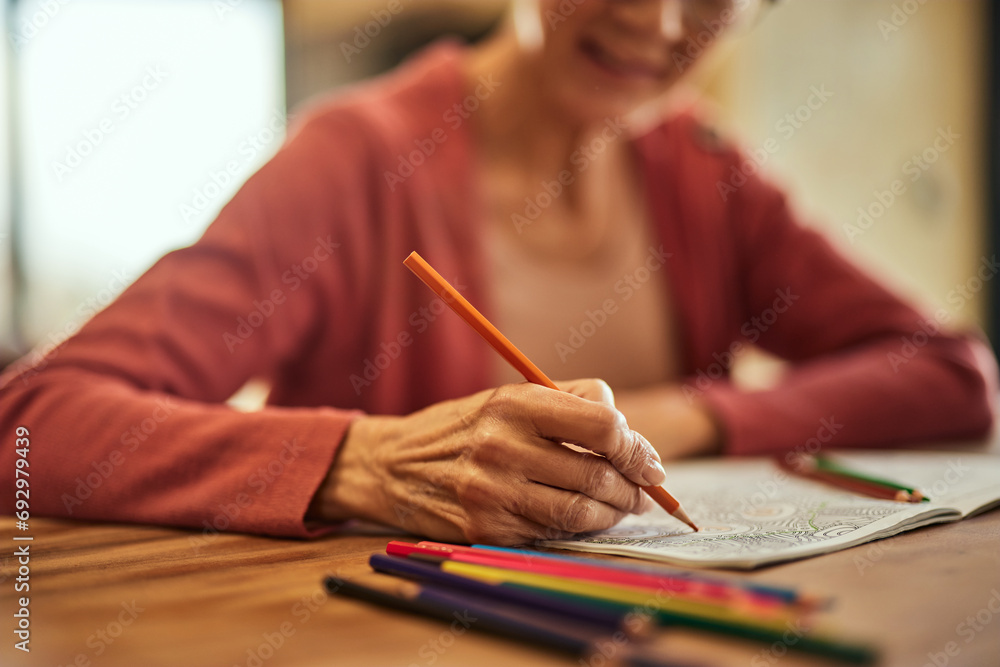 An older woman using a crayon and coloring the coloring book, close-up of the hand. An older woman using a crayon and coloring the coloring book, close-up of the hand.