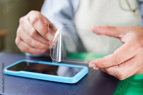Unrecognizable woman removes a transparent plastic film that covers the anti-scratch screen protector that she is going to install on a smartphone. photo
