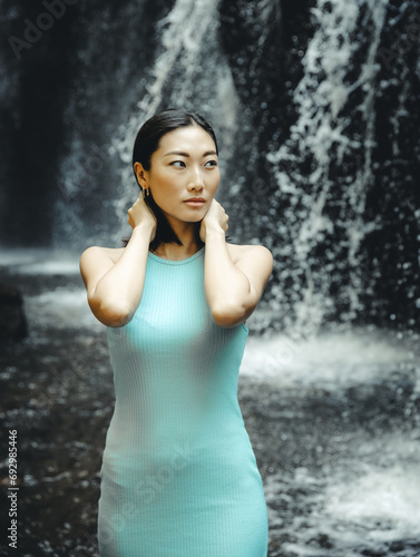 Portrait of Asian woman posing near the waterfall. Nature and environment concept. Travel lifestyle. Attractive woman wearing light blue dress. Copy space. Yeh Bulan waterfall in Bali