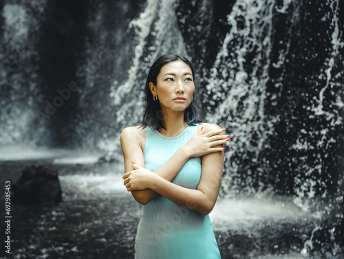 Portrait of Asian woman posing near the waterfall. Nature and environment concept. Travel lifestyle. Beautiful woman wearing light blue dress. Copy space. Yeh Bulan waterfall in Bali photo