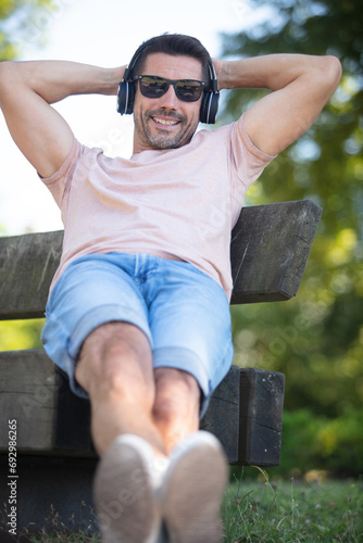 Принти на полотні man wearing headphones relaxing on a park bench