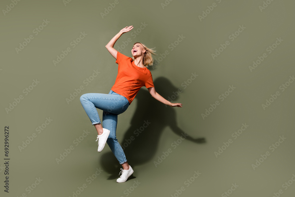 Full body photo of attractive young woman energetic excited dancing party wear trendy orange clothes isolated on khaki color background
