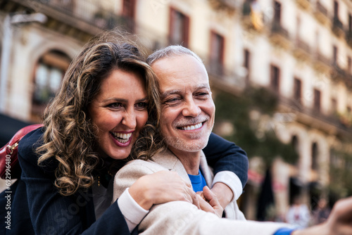 Affectionate mid adult woman hugging man having fun together in romantic date. Lovely mature couple bonding together taking a selfie in the street