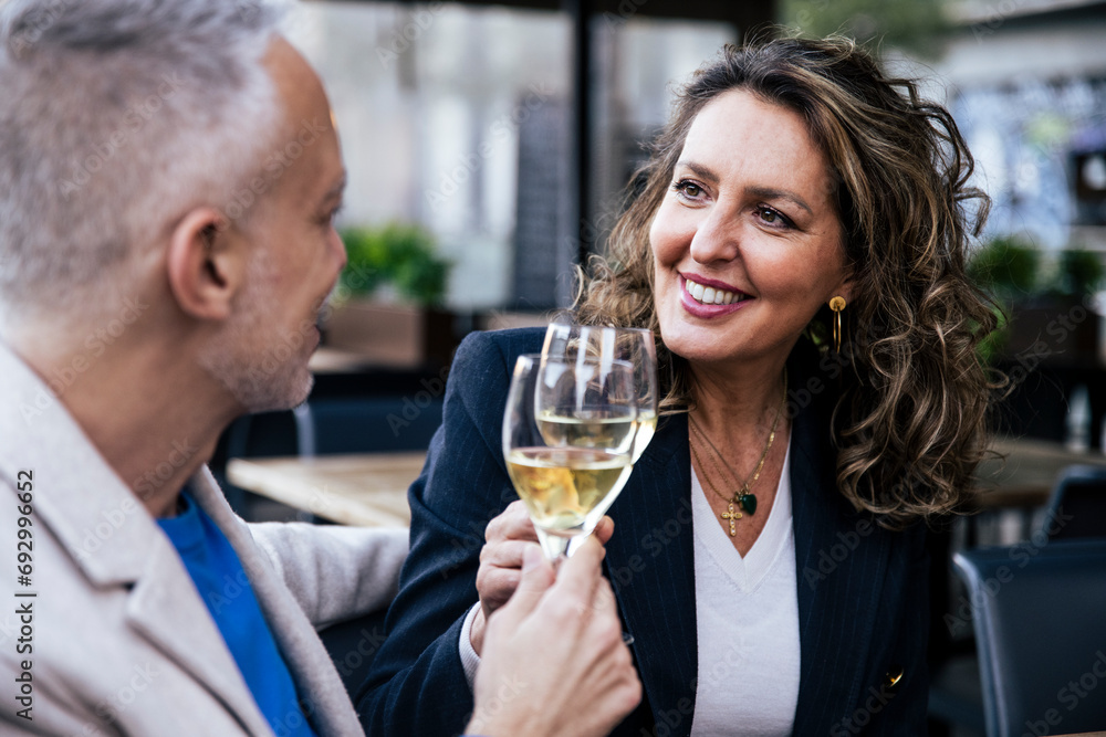 Smiling couple toasting with wine while sitting in a restaurant. Happy middle age woman and man drinking at a terrace looking each other. Smiling couple toasting with wine while sitting in a restaurant. Happy middle age woman and man drinking at a terrace looking each other.