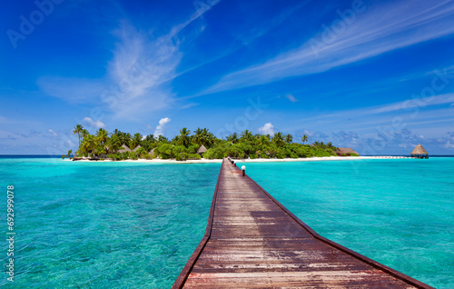 Long wooden jetty over blue ocean to tropical island beach