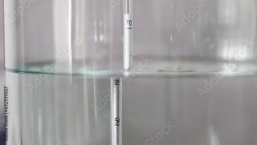 alcohol distilling process closeup - liquid distilled transparent liquid flowing in large glass jar with floating alcoholometer in it.