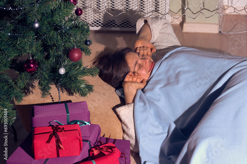 A woman in home clothes wakes up on Christmas morning under a mowed Christmas tree next to gifts