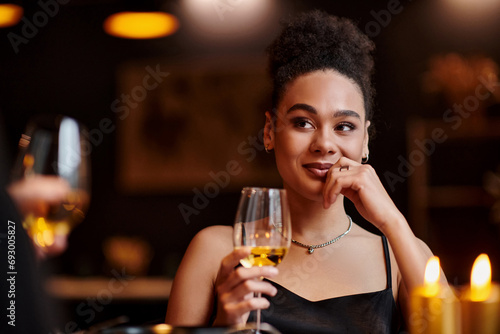 cheerful african american woman smiling and holding glass of wine during date on Valentines day