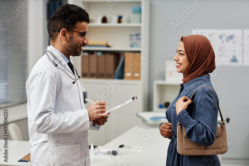 Bild auf Leinwand Side view at cheerful Middle Eastern male general practitioner and female patien