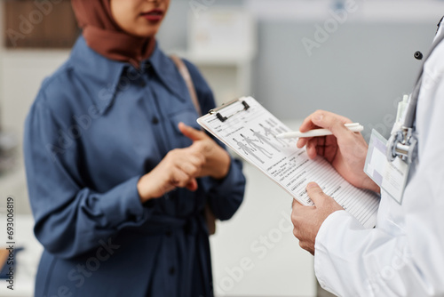 Cropped shot of male doctor filling medical card listening to female patient talking about symptoms of disease