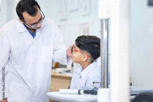 Indian child choosing eyeglasses in optics store, Boy doing eye test checking examination with optometrist in optical shop, Optometrist doing sight testing for child patient in clinic