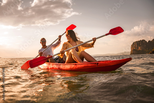 Fototapete Happy young couple is having fun and walking on kayak at sunset sea