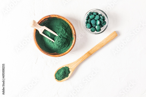 Wooden bowl,spoon and scoop filled with green spirulina algae powder on white background. A glass jar with spirulina tablets. Top view. Detox