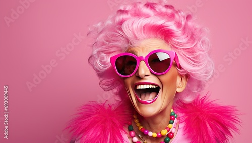 An elderly Caucasian woman with pink hair in pink glasses and bright clothing happily smiles against a pink background. The concept of an active lifestyle in the elderly