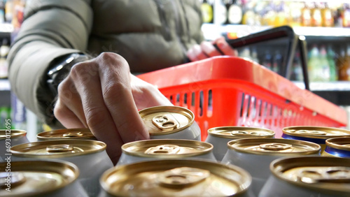 Fotografía Close-up of the hand of a man with a shopping basket taking a golden-white can o