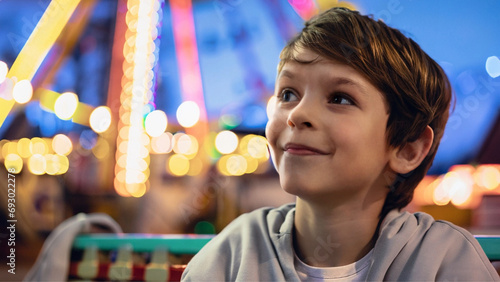 Close em um menino alegre, em um parque de diversões. com luzes coloridas desfocadas ao fundo. photo