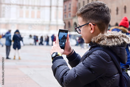 Boy enjoying view on the The Basilica of San Petronio at the center of Bologna . Concept of traveling famous landmarks in Italy. Caucasian Boy tourist making a photo with a phone 