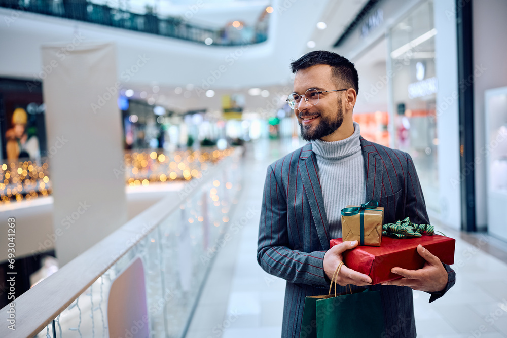 Fototapeta premium Happy man carrying gift boxes walking through shopping mall.