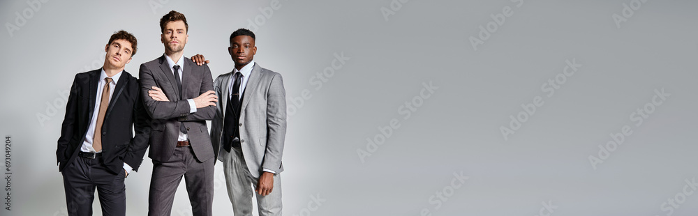 appealing interracial friends in smart business suits posing together on gray background, banner