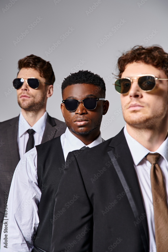 handsome multiracial male models in elegant smart suits with sunglasses posing on gray backdrop handsome multiracial male models in elegant smart suits with sunglasses posing on gray backdrop