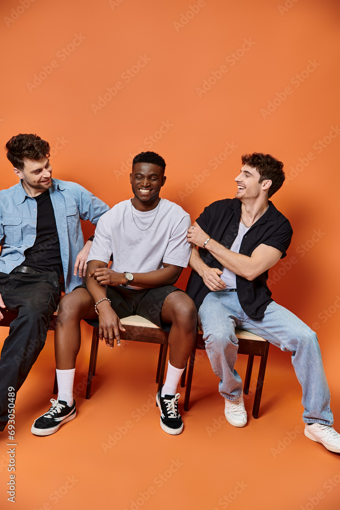 jolly interracial men in casual street outfits smiling happily on orange backdrop, fashion concept jolly interracial men in casual street outfits smiling happily on orange backdrop, fashion concept