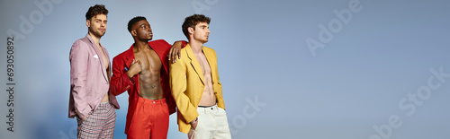 appealing diverse men in unbuttoned vibrant suits posing on gray backdrop, fashion concept, banner
