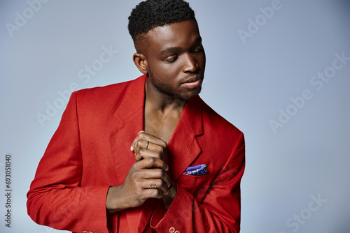 stylish african american man with vivid red blazer posing on gray backdrop, fashion concept photo