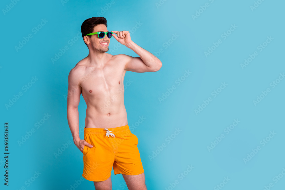 Photo portrait of handsome young guy pose look empty space dressed stylish yellow shorts isolated on blue color background summer vacation