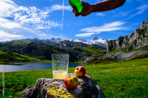 Pouring of natural Asturian cider made from fermented apples from green bottle and high height with view on Covadonga lake and tops of Picos de Europa mountains, Spain
