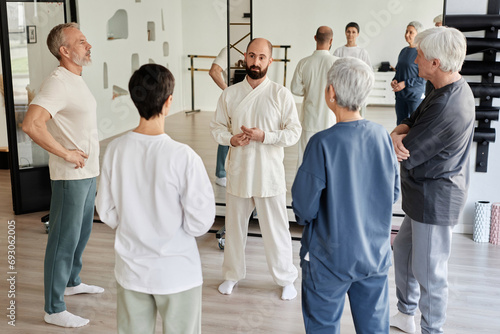 High angle view of elderly people looking at male master in white outfit explaining importance of qigong exercises for health, group back facing camera photo