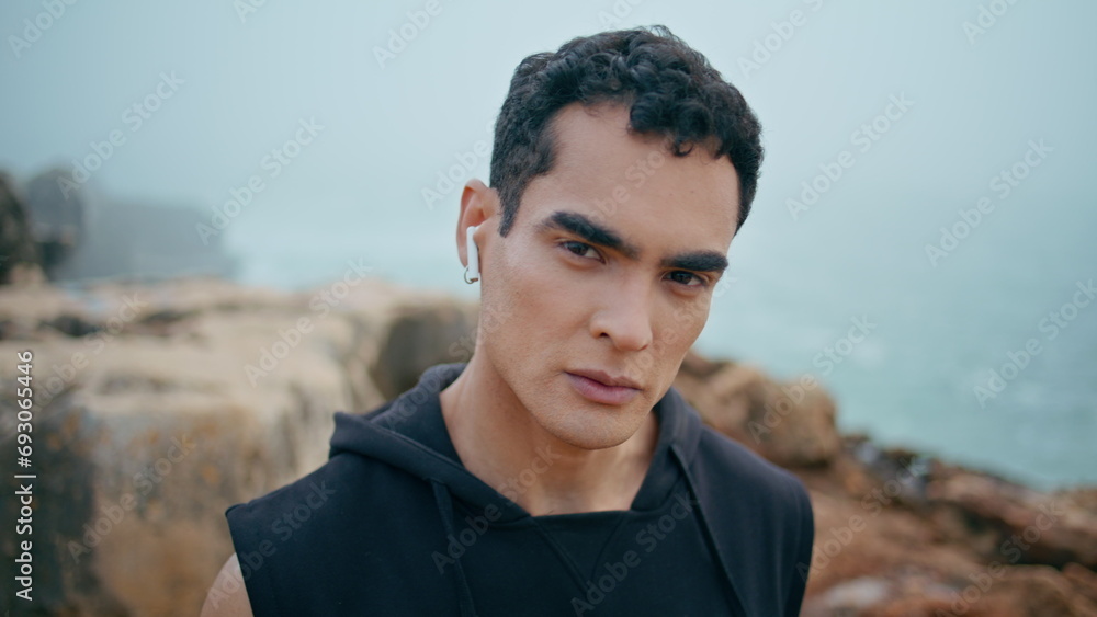 Male athlete looking camera at cloudy seaside closeup. Handsome fit guy listen Male athlete looking camera at cloudy seaside closeup. Handsome fit guy listen