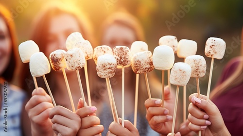Close up of hands roasting marshmallows on stick in the warmth of an evening campfire photo