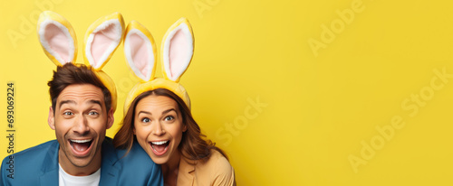 Two people, a happy couple, adorned with Easter bunny ears, express their delight against a sunny yellow backdrop while celebrating Easter, banner, copyspace