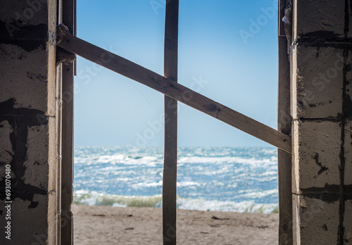 cross of boards in the window overlooking the sea and the beach © Sofiia
