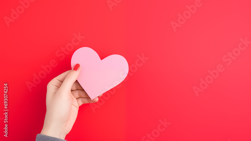 Hand holding blank paper greeting or invitation card over red background with heart shape. Christmas, Valentine day, New Year, winter holidays concept.