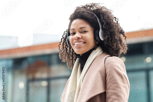 Portrait of friendly black woman using headphones and looking at camera.