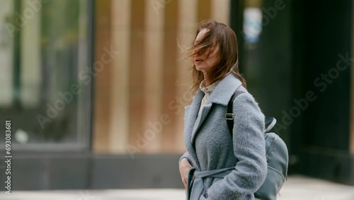 attractive middle-aged lady in warm coat walking alone in city street, portrait in motion, side view photo