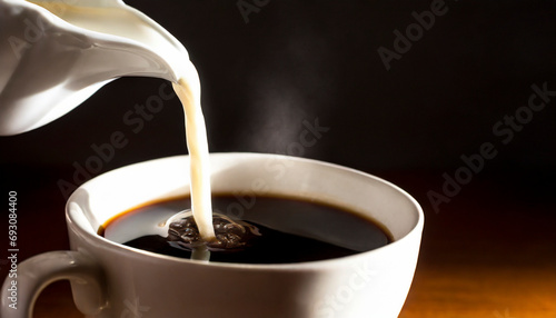 Pouring milk into a cup of coffee on a black background.