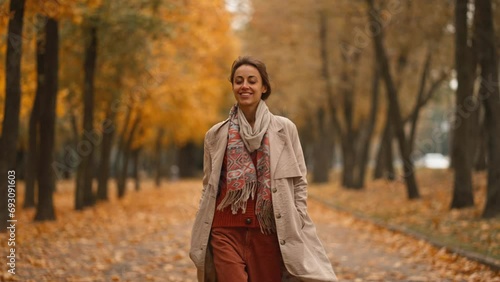 Portrait of an attractive brunette woman walking in the park at fall on a sunny day and smiling. The face of a happy beautiful woman in autumn outdoor. Slow-motion 4k footage