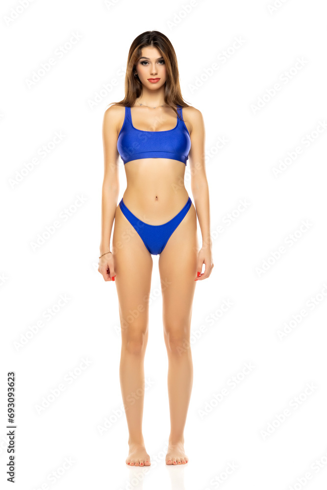 Young beautiful brunette woman in blue bikini swimsuit posing on a white studio background. Young beautiful brunette woman in blue bikini swimsuit posing on a white studio background.
