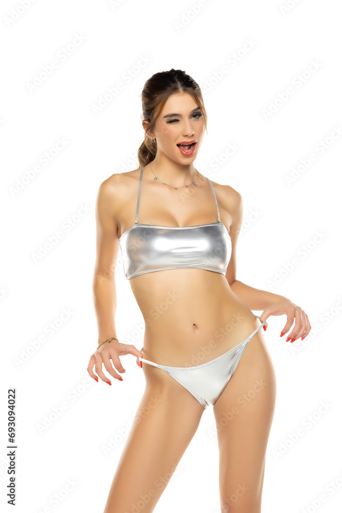 Young beautiful brunette woman in metalic silver bikini swimsuit posing on a white background. Young beautiful brunette woman in metalic silver bikini swimsuit posing on a white background.