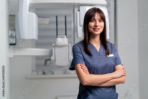 portrait of a beautiful young female doctor dentist or radiologist in uniform standing with crossed arms in the beauty and health clinic photo